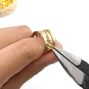 Macro view of pliers assembling golden jump rings onto a multi-layer DIY metal ring base