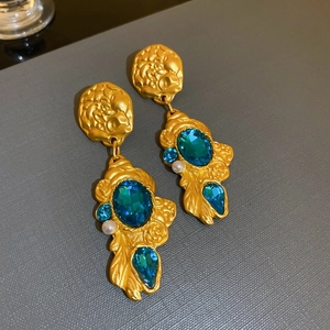 Detail of vintage matte gold earrings with blue gemstones and white pearl accents
