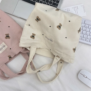 Close-up of pink and beige corduroy tote bags featuring cute bear embroidery details