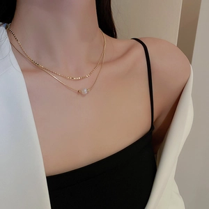 Close-up of layered golden chain necklace with white pearl pendant on model neck