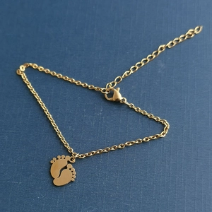 Polished stainless steel bracelet with gold-plated baby footprint charms on blue background