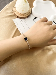 Close-up of elegant gold bracelet featuring a large blue square zircon and clear crystals