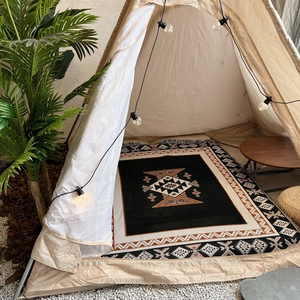 Detailed view of a Bohemian woven picnic rug inside a cozy beige pyramid camping tent