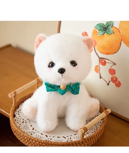 Close-up of white puppy plush with green polka dot bowtie in a cozy woven tray