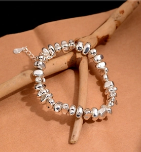 Detail of irregular silver bead bracelet on a dry branch with soft lighting