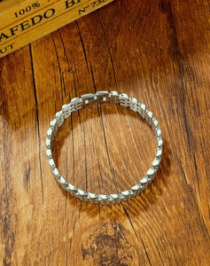 Detailed view of silver stainless steel watch-style bracelet links on a dark wood surface