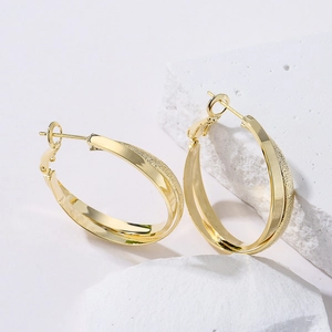 Polished and frosted gold-plated geometric hoop earrings displayed on a white stone block