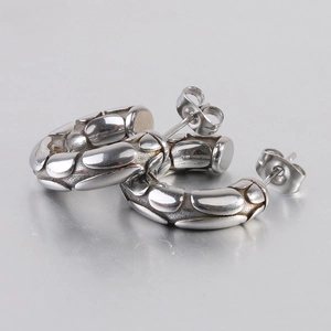 Close-up of silver C-shaped hoop earrings with embossed pebble texture and butterfly clasp