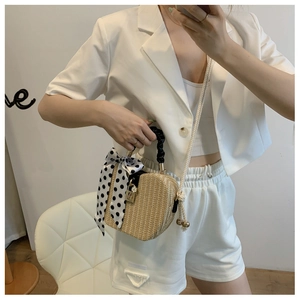 Detail of beige straw box bag featuring black twisted handle with polka dot silk scarf