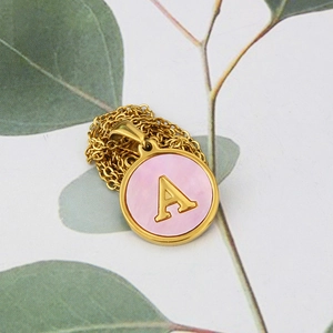 Detail of golden stainless steel necklace with pink shell pendant and A letter engraving