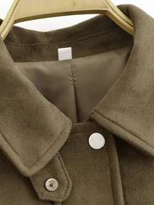 Détails de la veste en daim marron montrant les coutures du revers et les boutons pression
