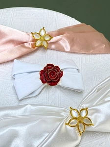 Close-up of elegant gold flower napkin rings with white enamel petals and red roses