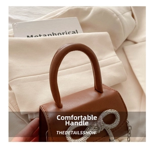 Close-up of brown leather handbag featuring a large rhinestone bow and metal chain strap