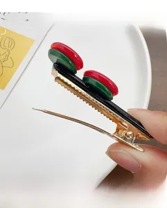Close-up of a retro duckbill hair clip with red and green acrylic beads on golden metal base