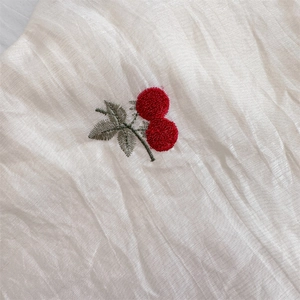 Detailed close-up of cherry embroidery on off-white textured fabric shoulder bag