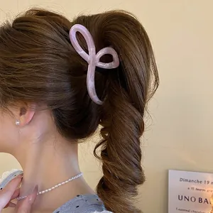 Pink marble texture claw clip in abstract bow design on dark brown hair in warm light
