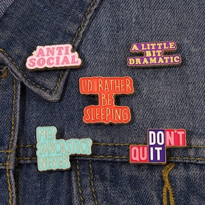 Close-up of five colorful enamel pins with funny slogans on blue denim fabric texture
