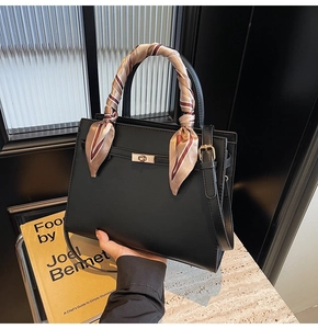 Detail of a chic black structured handbag featuring a metal twist lock and silk scarf handle