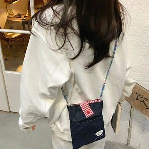 Detail of denim crossbody bag featuring rainbow beaded strap and cartoon dog embroidery