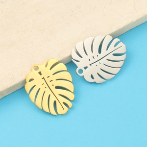 Close-up of gold and silver hollow monstera leaf pendants in polished stainless steel