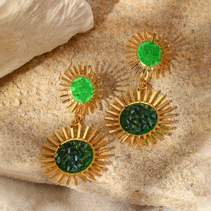 Macro shot of gold sunburst earrings with emerald green zircon inlay on rustic stone