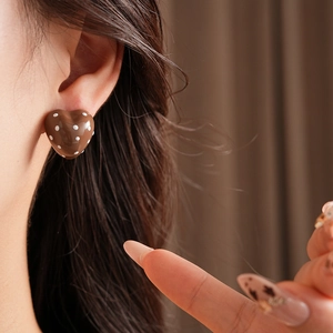 Close-up of heart-shaped brown earrings with white polka dots worn by a model