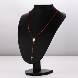 Chapelet à perles rouges avec croix dorée présenté sur un buste de mannequin noir