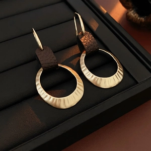 Detail shot of golden hammered metal rings and brown leather earrings in a black box