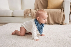 Blue waterproof cotton baby bib with animal pattern worn by crawling infant on rug