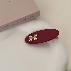 Macro view of burgundy oval hair clip with gold bow and metallic alligator clasp