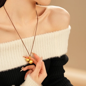 Close-up of golden gourd pendant on brown cord necklace worn by a fashion model