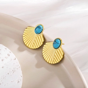 Close-up of fan-shaped gold earrings with turquoise stones on white ceramic and silk