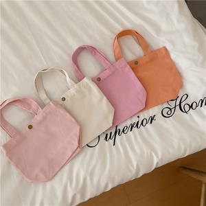 Flat lay of small canvas tote bags in pink, cream, purple, and orange with snap buttons