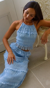 Close-up of light blue pleated sleeveless top and tiered ruffle skirt with textured fabric