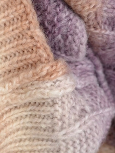 Close-up of cable knit sweater fabric with soft pink, cream and lilac gradient texture