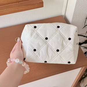 Détail d'une trousse de maquillage blanche à pois avec surpiqûres en losange et fermeture