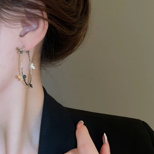 Close-up of large silver hoop earrings with black and white butterfly charms on a model