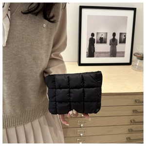 Close-up of black quilted down handbag held by model in a cozy interior setting