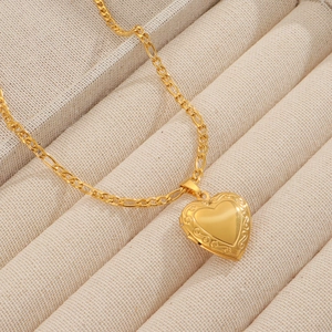 Close-up of golden heart locket necklace with vintage textured edges and Figaro chain