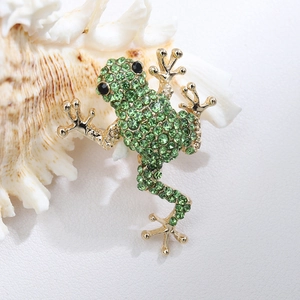 Close-up of golden frog brooch with green rhinestones resting on a cream seashell