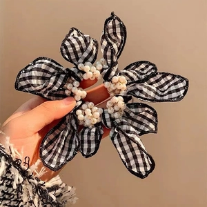Checkered bow hair scrunchie with pearls held in hand against a warm background
