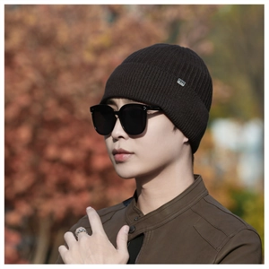 Detail of dark brown knitted beanie with vertical ribbed pattern and silver metal logo