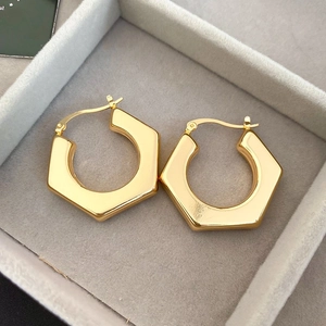 Macro detail of geometric hexagonal golden hoop earrings on a gray velvet jewelry tray