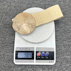 Detail shot of woven belt with gold round buckle showing a weight of 98.4g on a scale