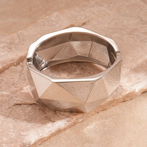 Detail of silver geometric wide bangle with radial faceted textures on stone base