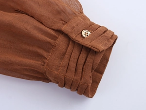 Detailed macro view of pleated cuffs on a brown dress with elegant gold button closure