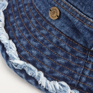 Macro detail of denim bucket hat featuring frayed edges and vintage metal logo button