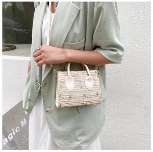 Model wearing a woven straw bag with green flower embroidery and white leather strap