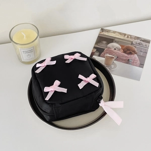 Detail of black makeup bag with four pink ribbon bows on top and a ribbon zipper pull