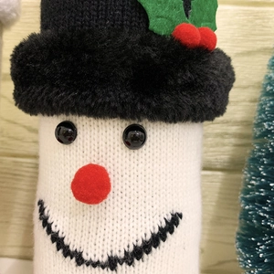 Knitted snowman wine bottle cover with a plush black hat and festive holly decoration